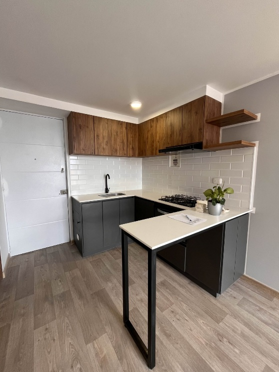 Pequeña cocina moderna con armarios de madera, salpicadero de azulejos blancos, encimeras negras y una mesa tipo península.