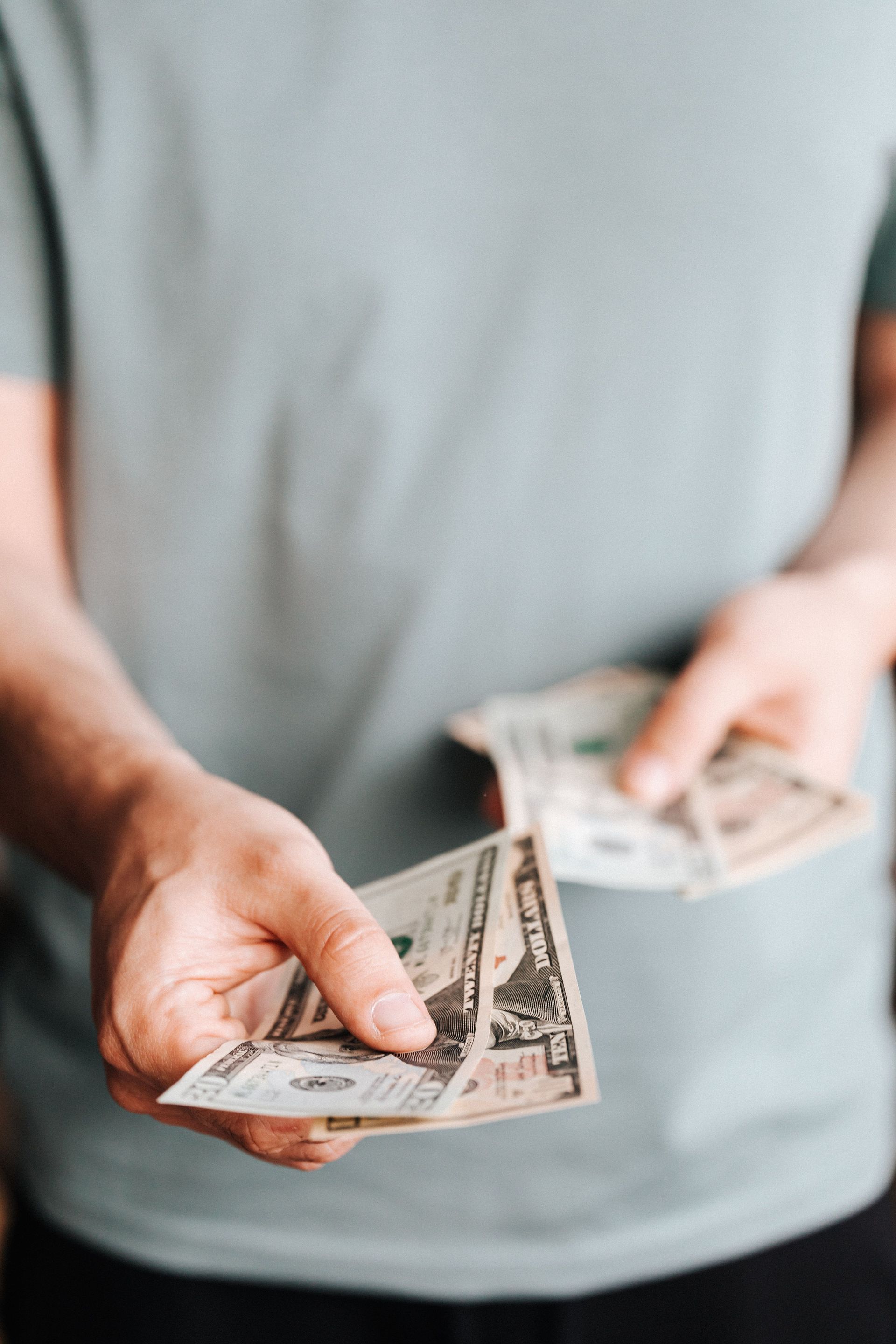 Person holding and counting U.S. dollar bills against a gray shirt
