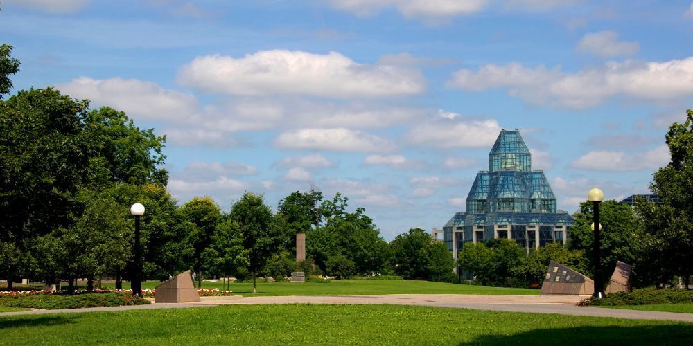 A large glass building is sitting in the middle of a park surrounded by trees.