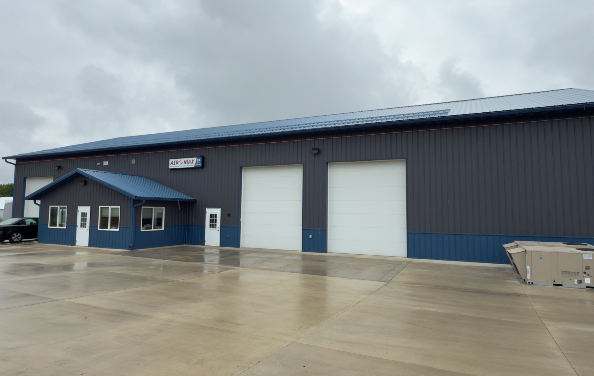 Dark blue industrial building with two garage doors, a small entrance, and a cloudy sky.