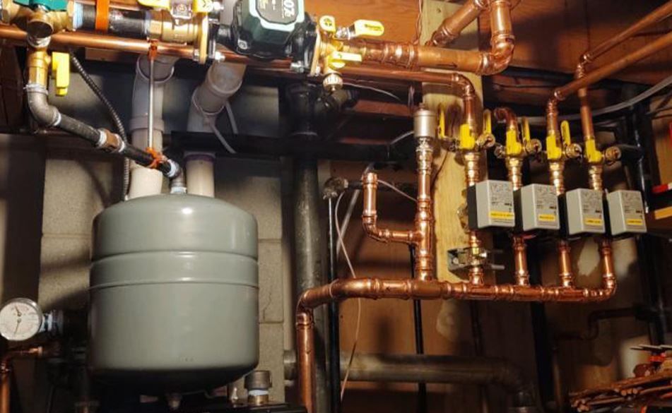 Copper plumbing system with gray expansion tank, pump, and multiple zone valves in a basement.