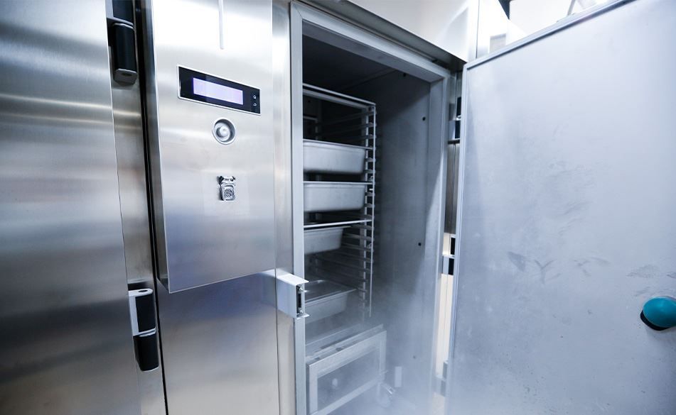 Open stainless steel freezer showing shelves with trays.