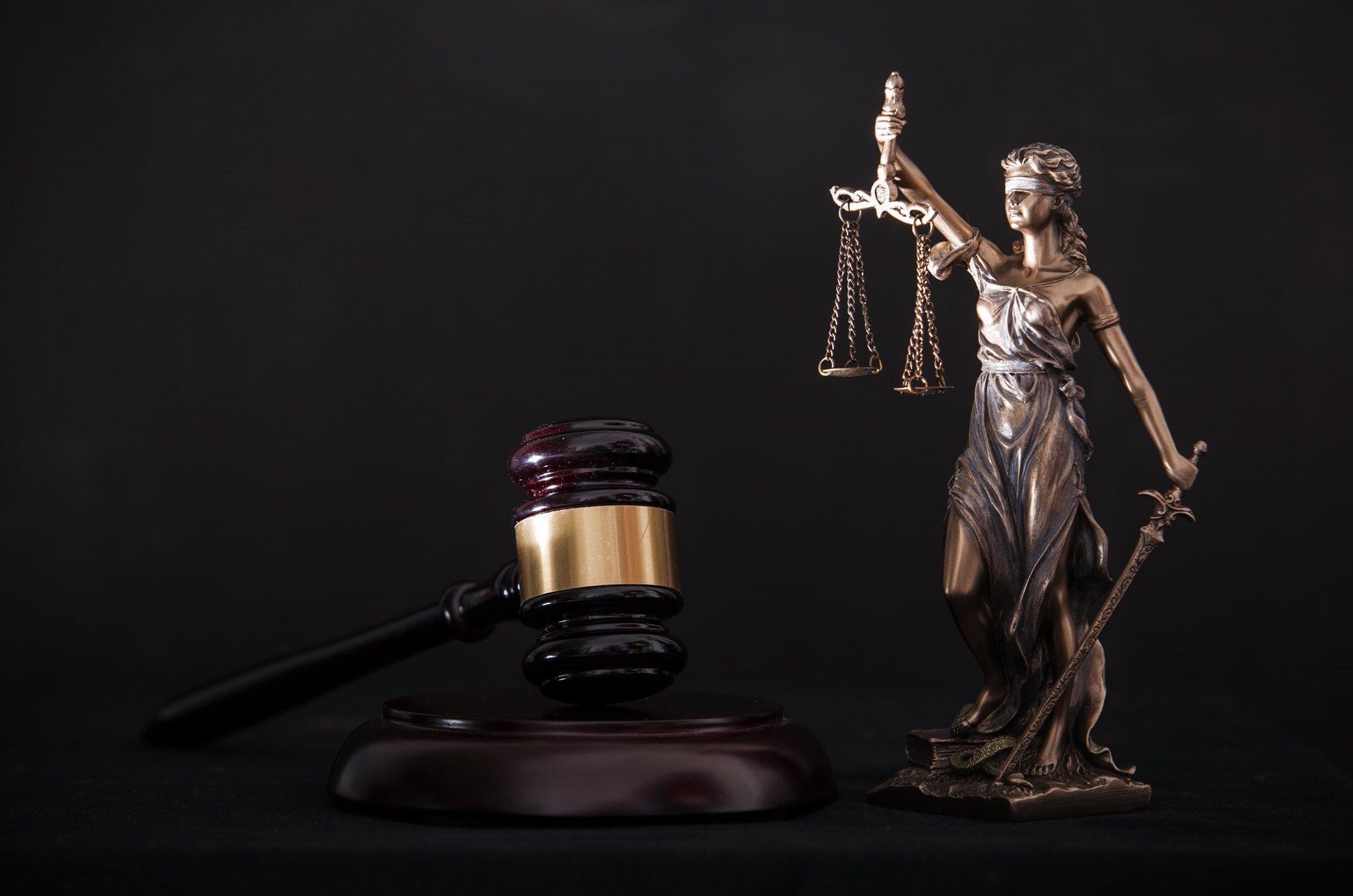 Gavel and statue of Lady Justice with scales and sword, on dark background.