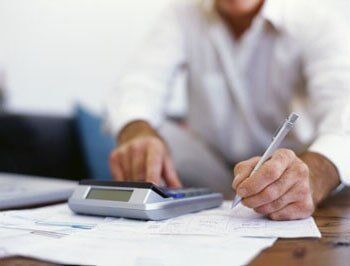 Person calculating with calculator, writing on paper; office setting.