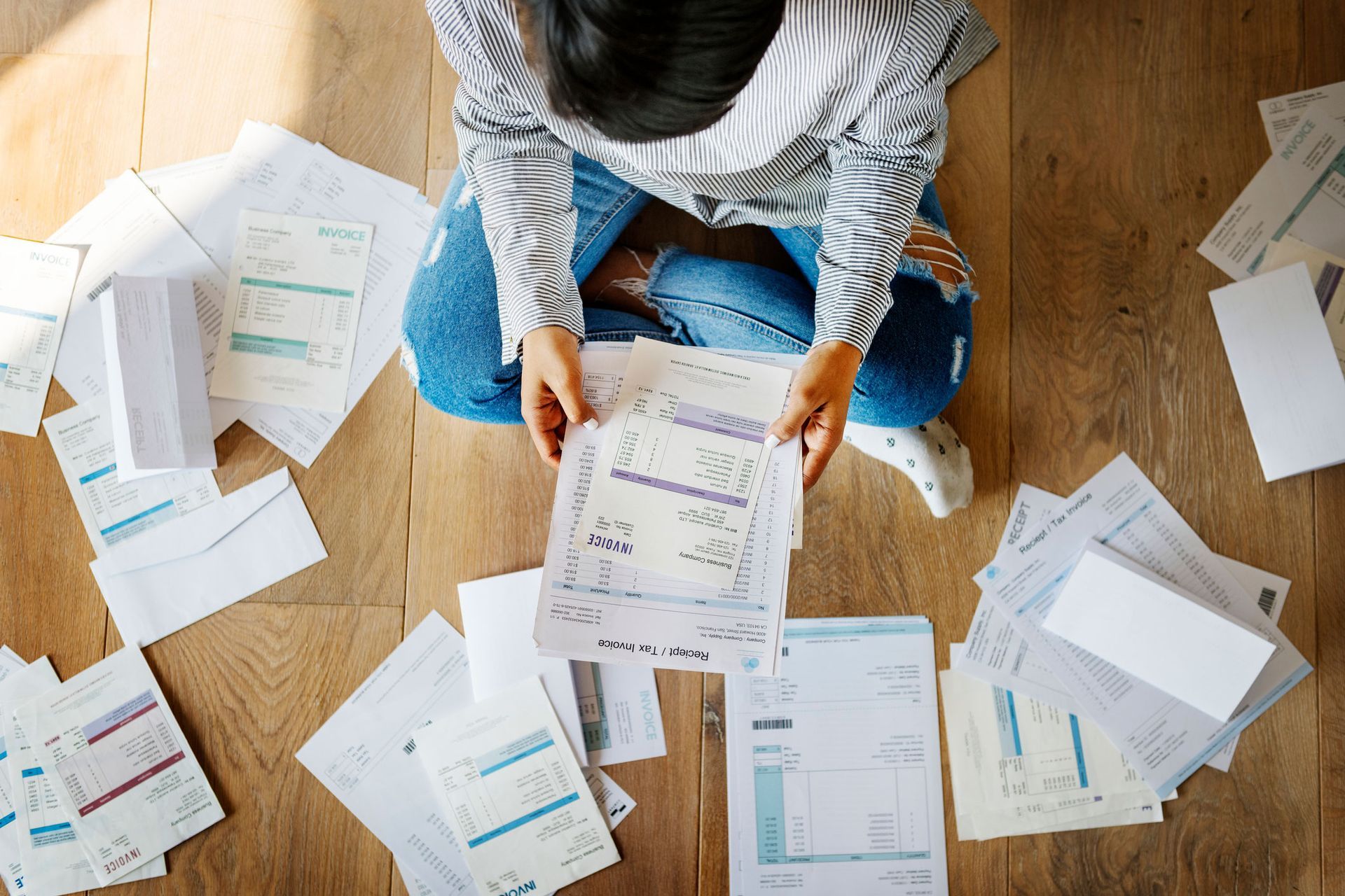 Person sitting on floor surrounded by bills, looking stressed.