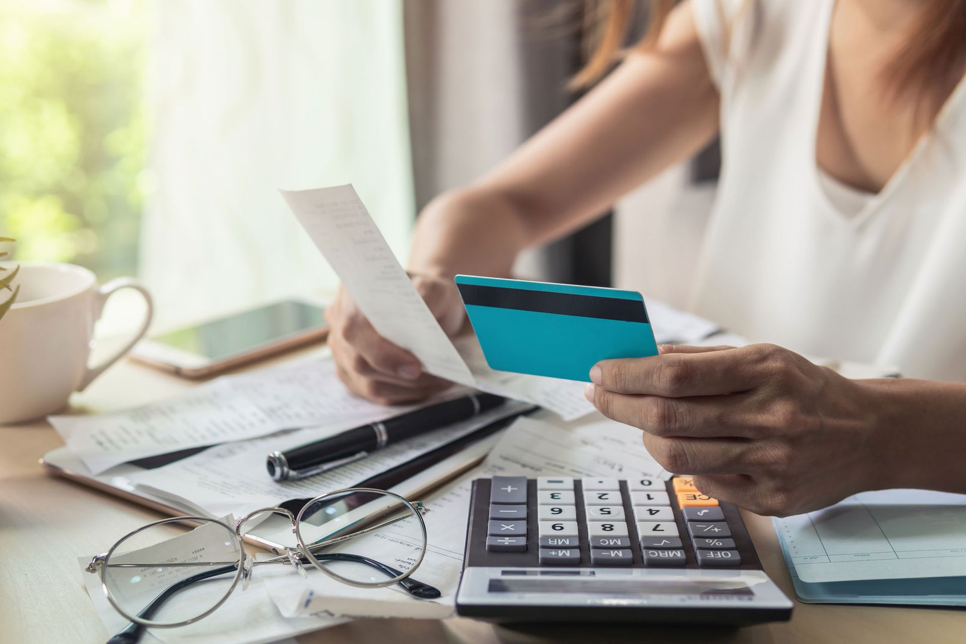 Person reviewing receipts, credit card in hand, with calculator and glasses on desk.