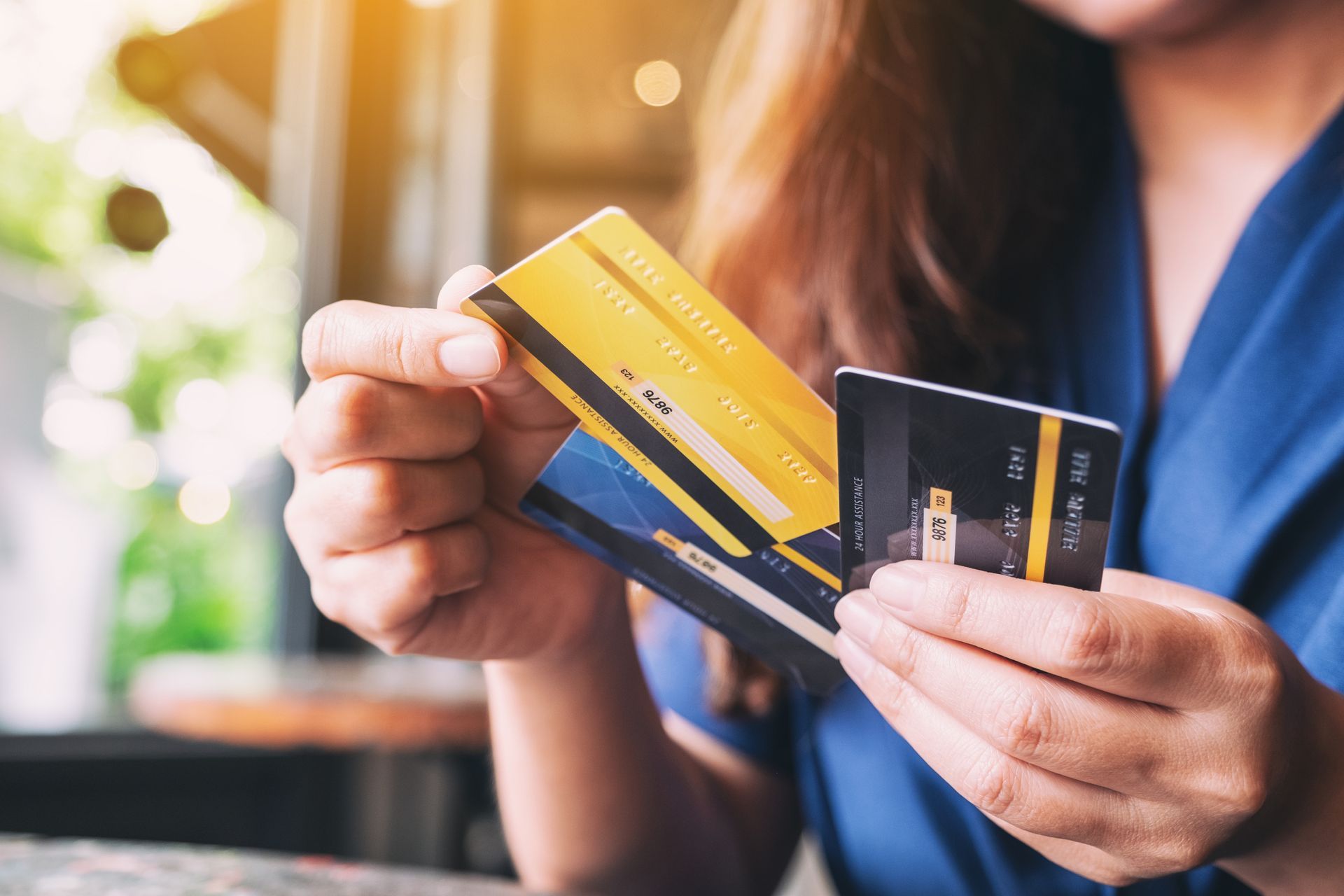 Woman holding a stack of credit cards, indoors, close-up. Cards are gold, blue, and black.