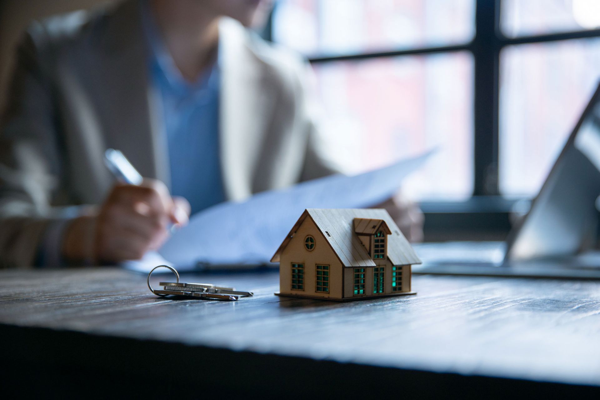 Model house and keys on desk with person signing documents.
