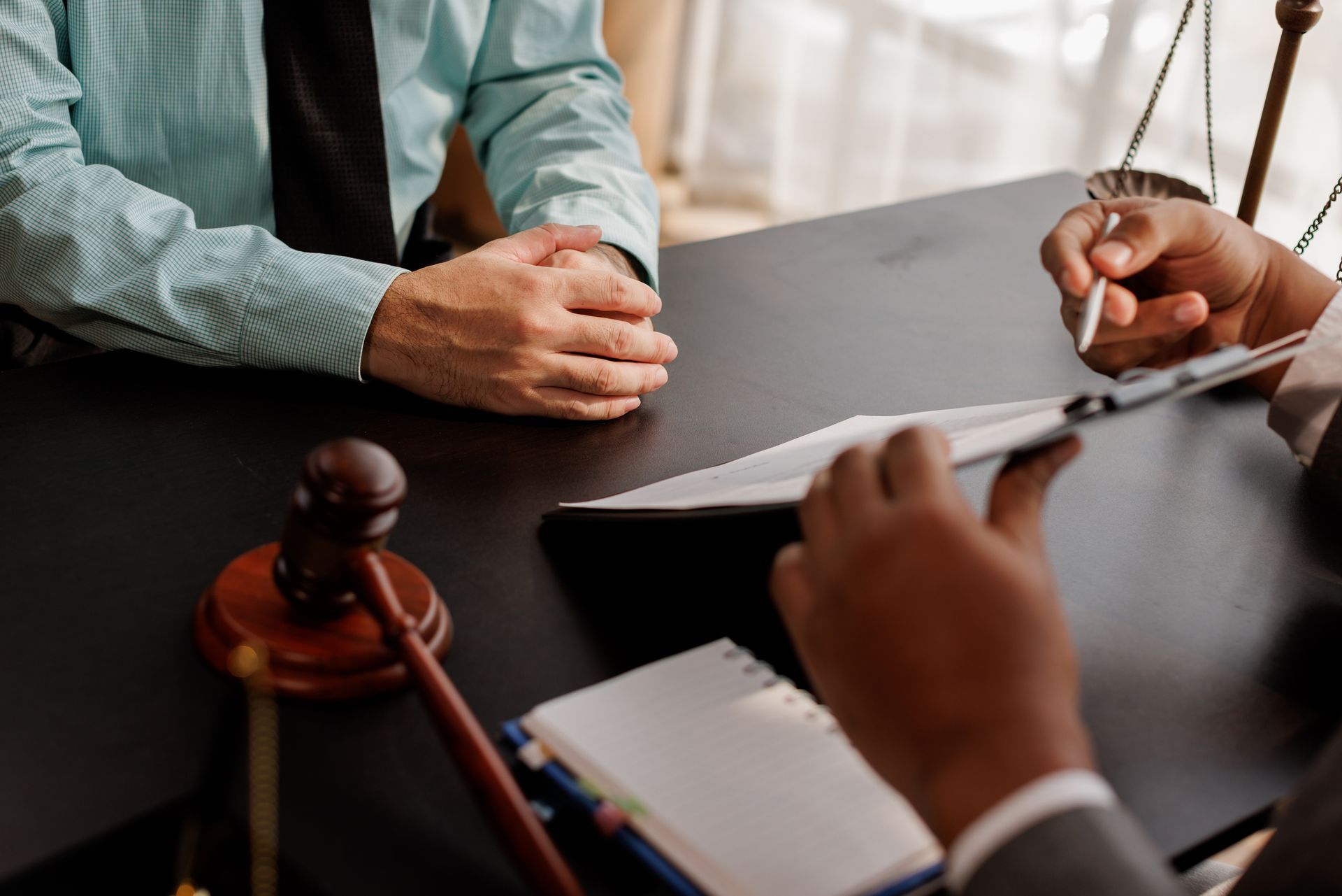 Two people at a desk, one with folded hands, another writing on a document. Gavel on the desk.