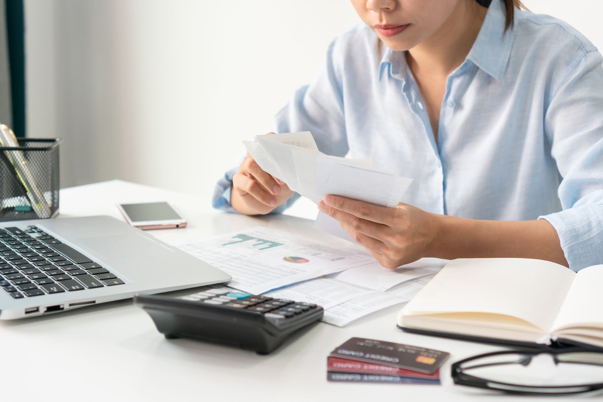 Woman reviewing documents at a desk, with laptop, calculator, and credit cards.