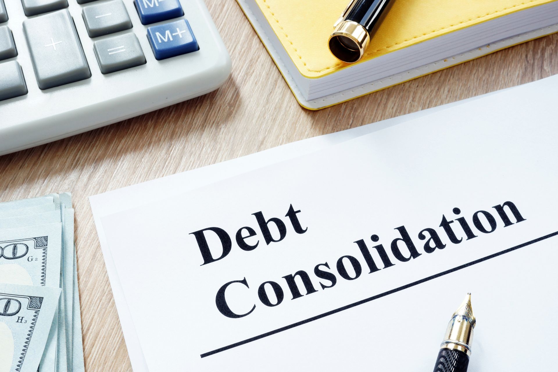 Debt consolidation form, notebook, calculator, and money on a desk. Debt consolidation document with calculator, notepad, pen, and cash on a wooden desk.