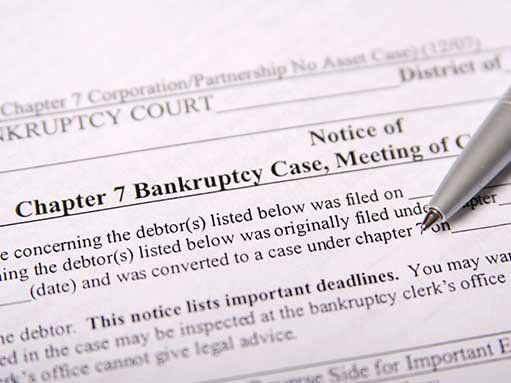 Close-up of a bankruptcy court notice with a pen resting on it. Text includes