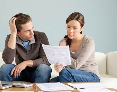 Couple looking at papers, appearing concerned, sitting on a couch.