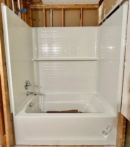White alcove bathtub with built-in shelves and subway tile design, installed in a framed-out bathroom space.