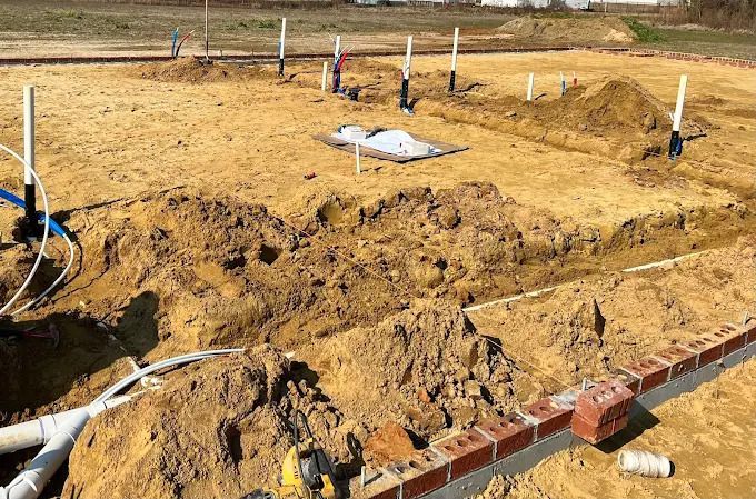 Construction site with foundation trenches, brick border, and plumbing.