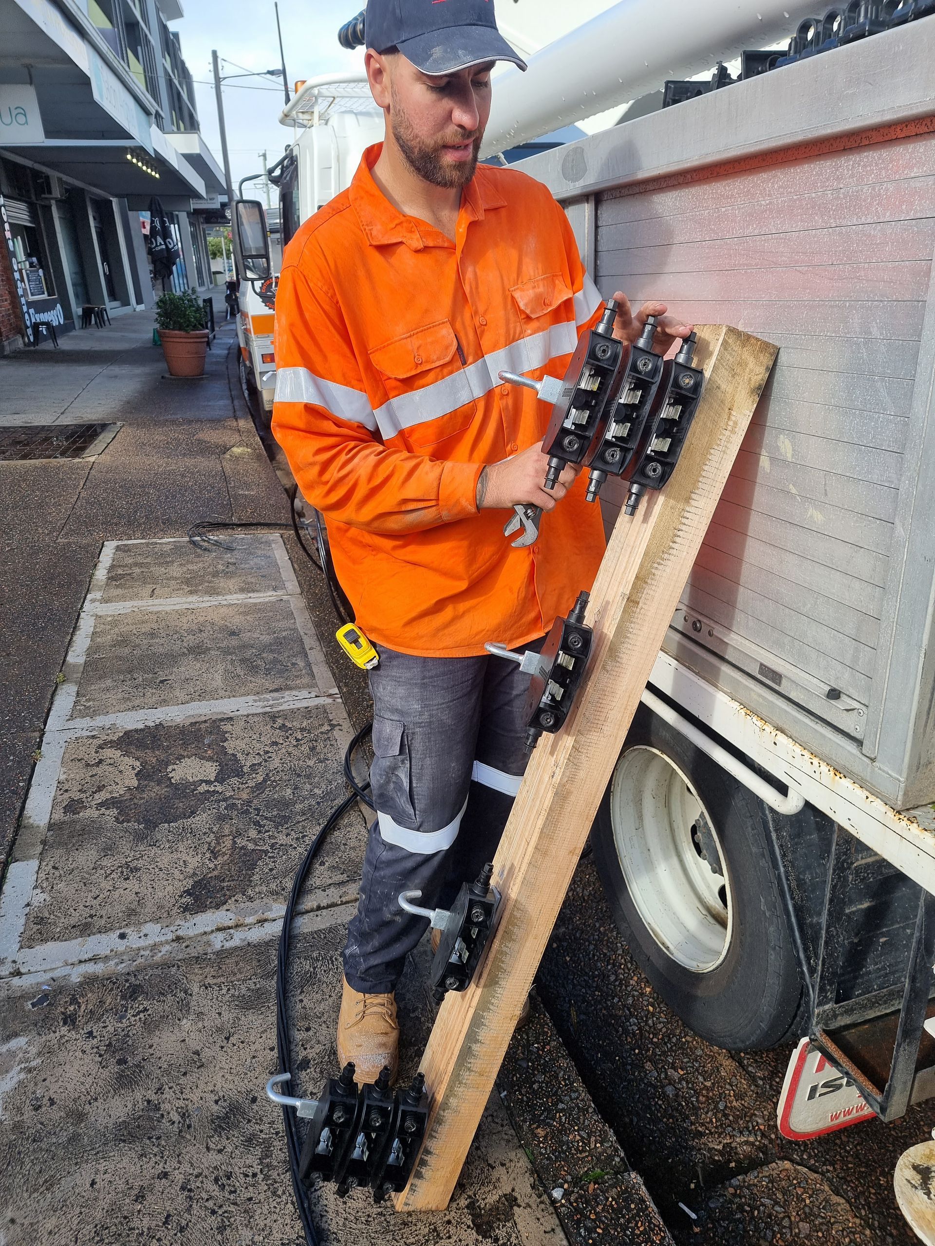 Worker in orange safety jacket handling a wooden rack beside a truck outdoors.