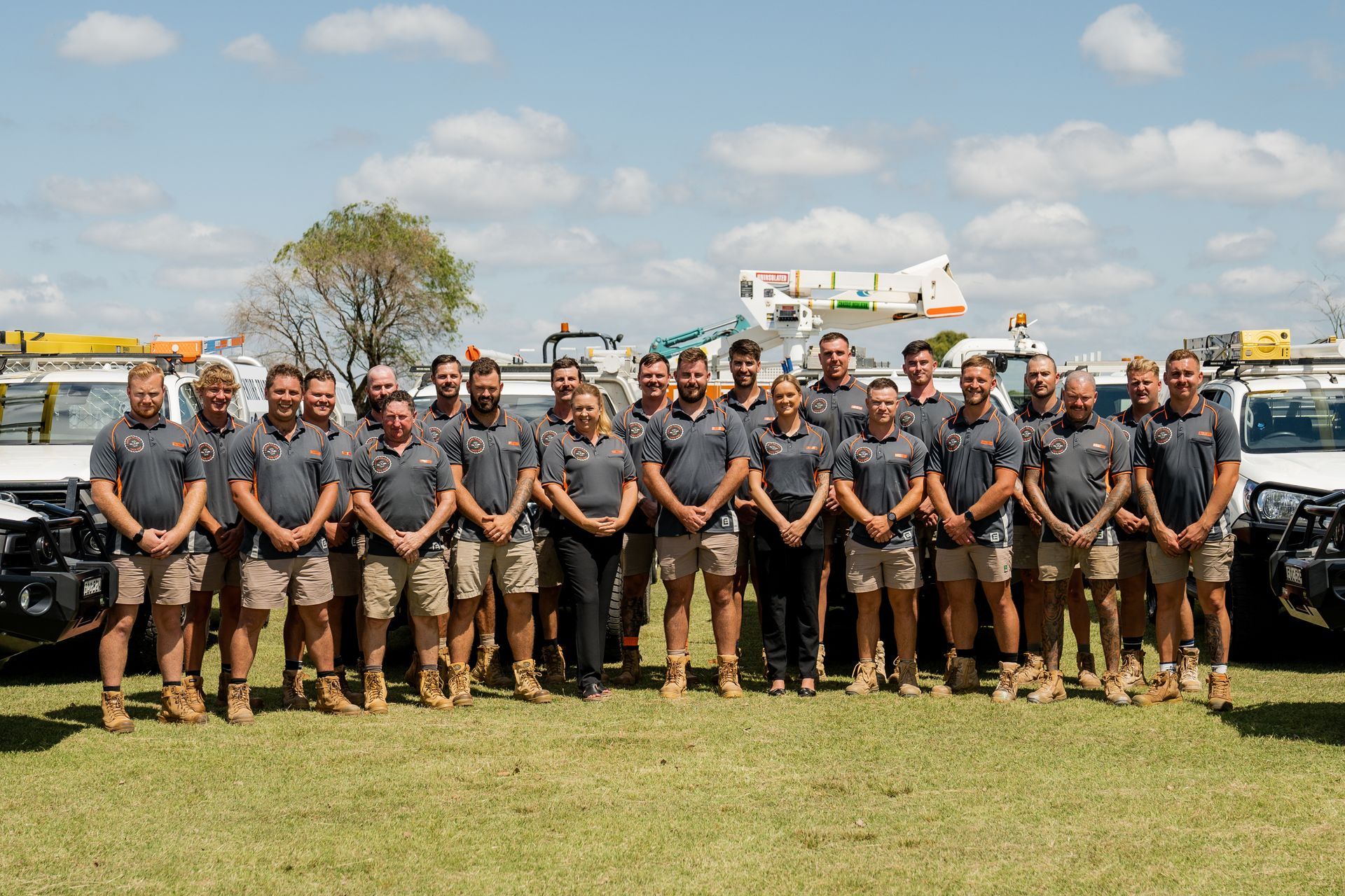 Group of volunteers posing in a field beside utility trucks and equipment under a partly cloudy sky