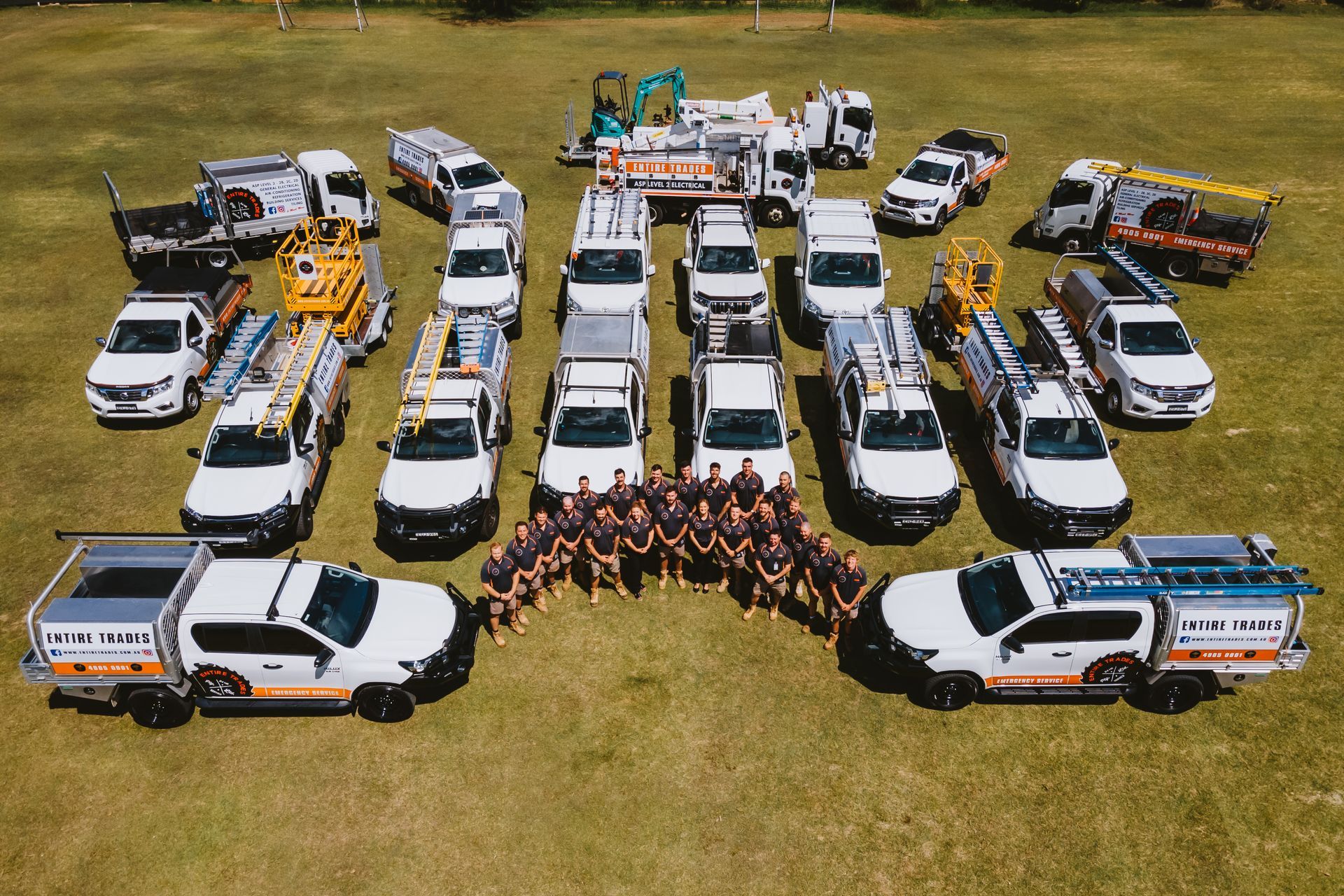 Group of volunteers posing in a field beside utility trucks and equipment under a partly cloudy sky
