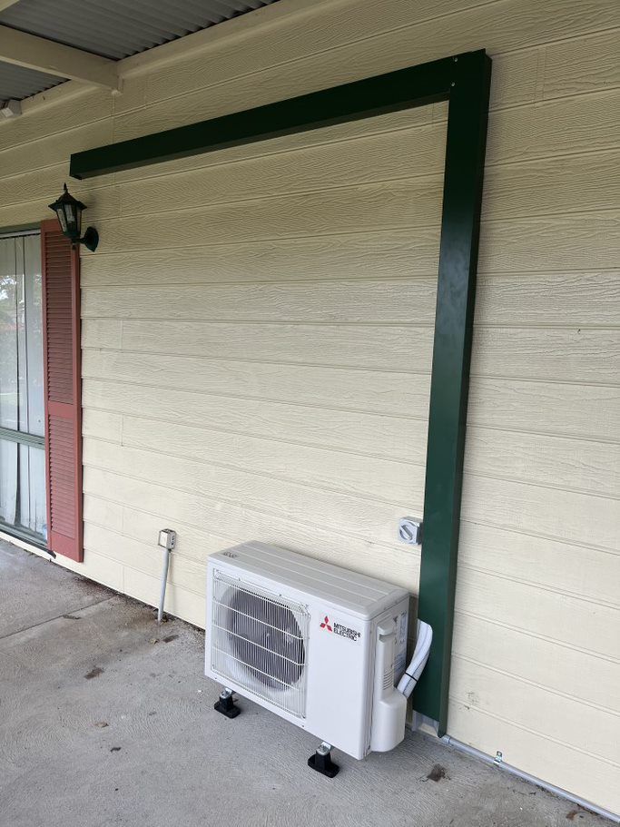 Outdoor wall-mounted mini-split air conditioner beneath a covered porch, with dark green trim.