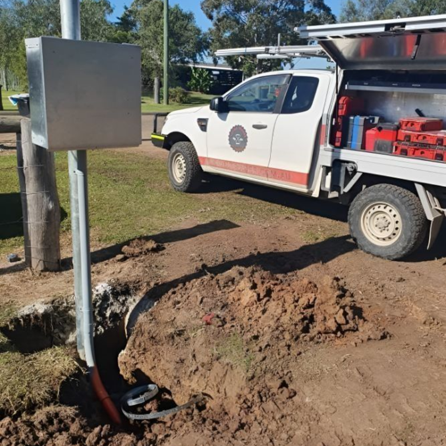 Utility truck beside open trench and metal electrical box at a roadside work site.