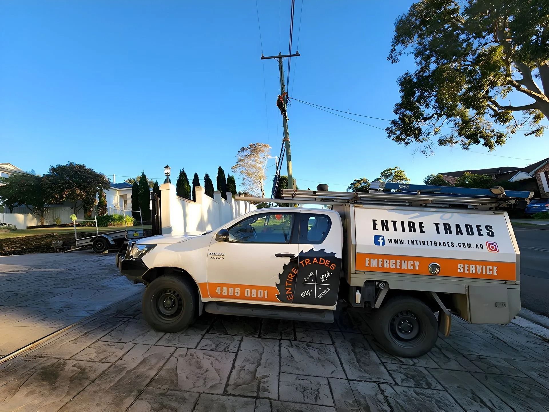 White utility truck parked by a white wall and palm trees, with orange and black company signage.