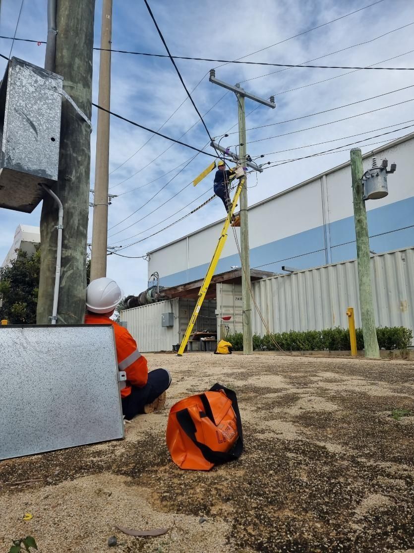 Worker in orange safety gear climbing a yellow ladder near power lines outdoors