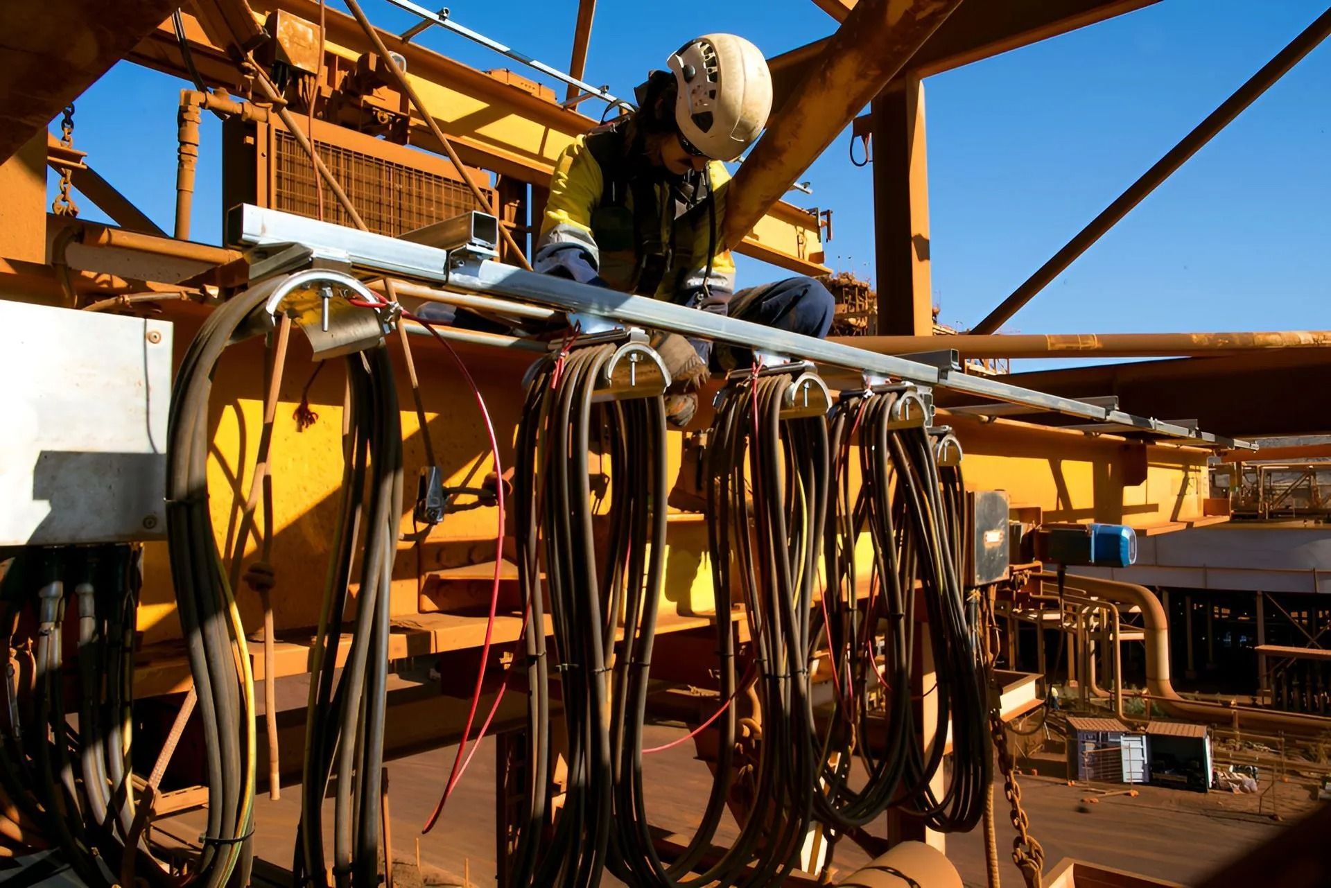 Industrial worker inspecting cables on a construction rig under a blue sky