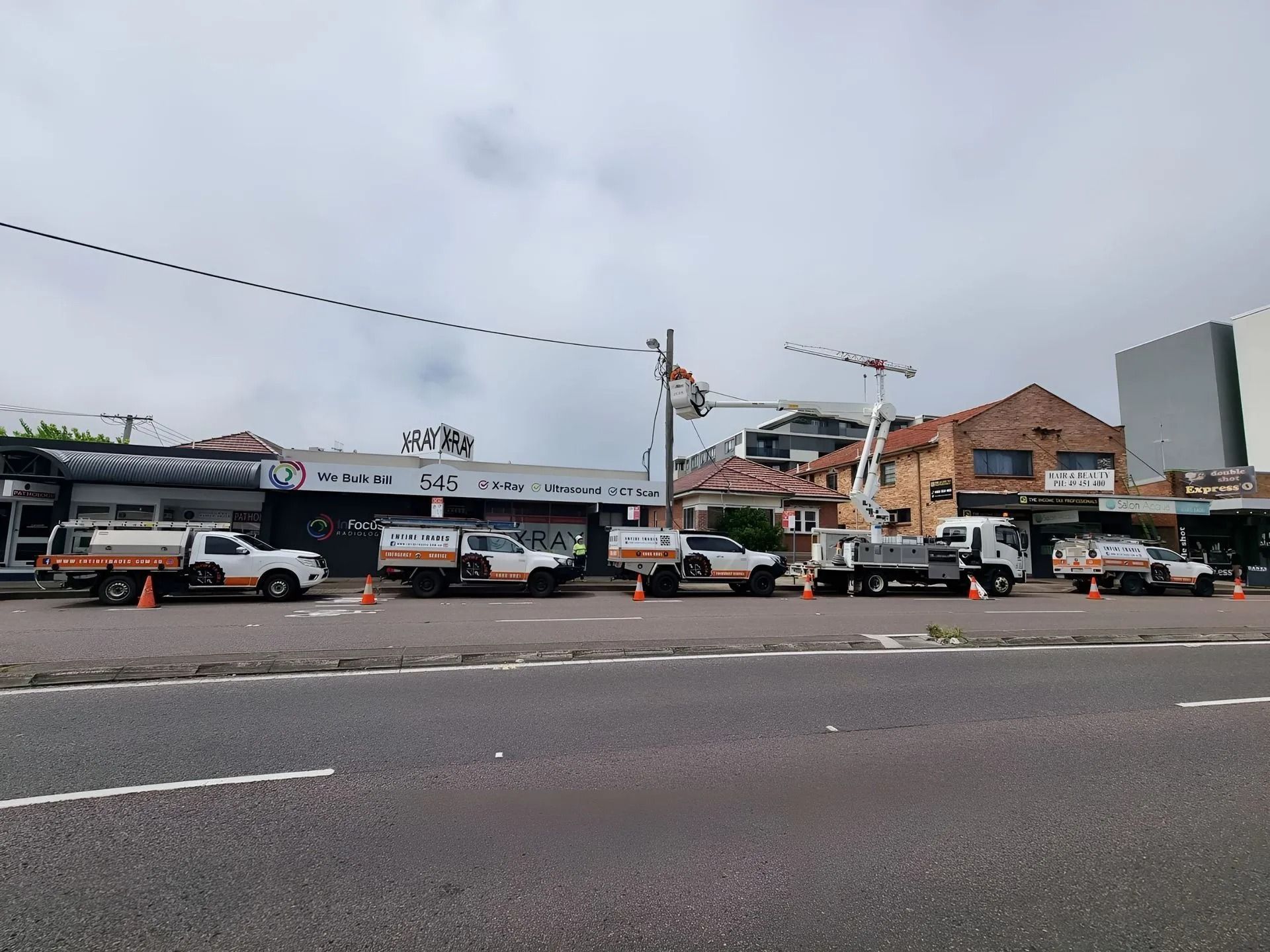 Street scene with buses, cars, and a brick building under a cloudy sky.