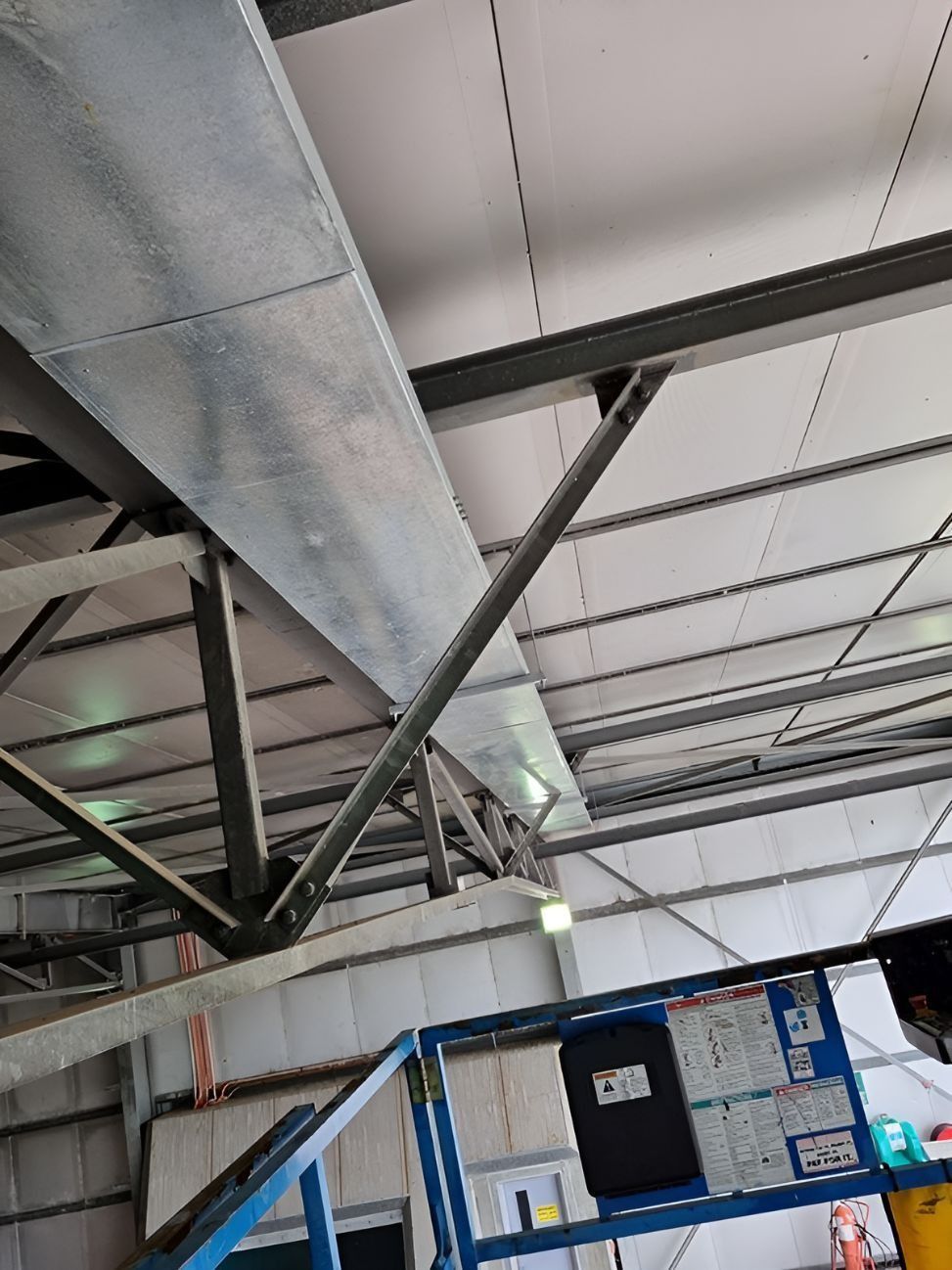 Industrial warehouse ceiling with metal beams, ductwork, and a suspended ceiling panel.