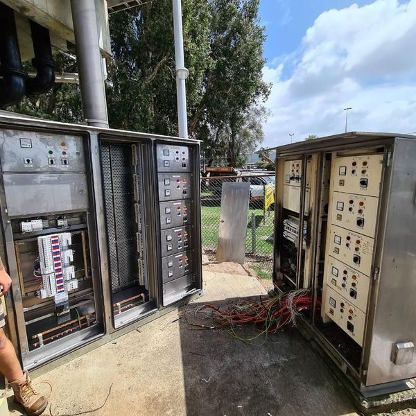 Open electrical control panels and wiring cabinets outdoors under a cloudy sky