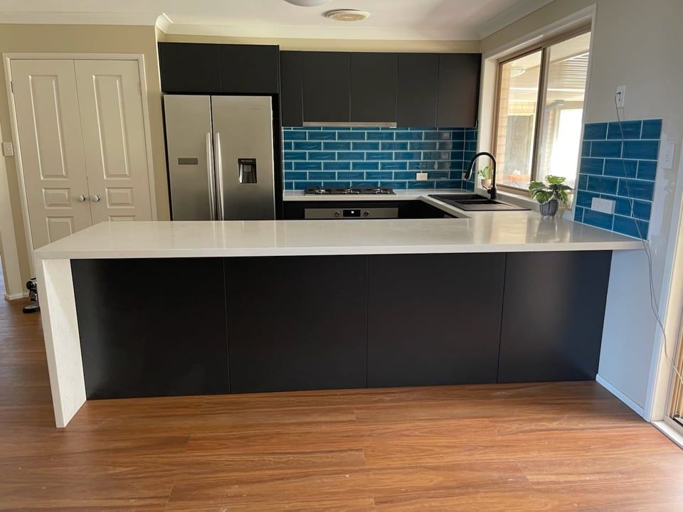 Modern kitchen with dark cabinets, white island, blue tile backsplash, and stainless steel appliances