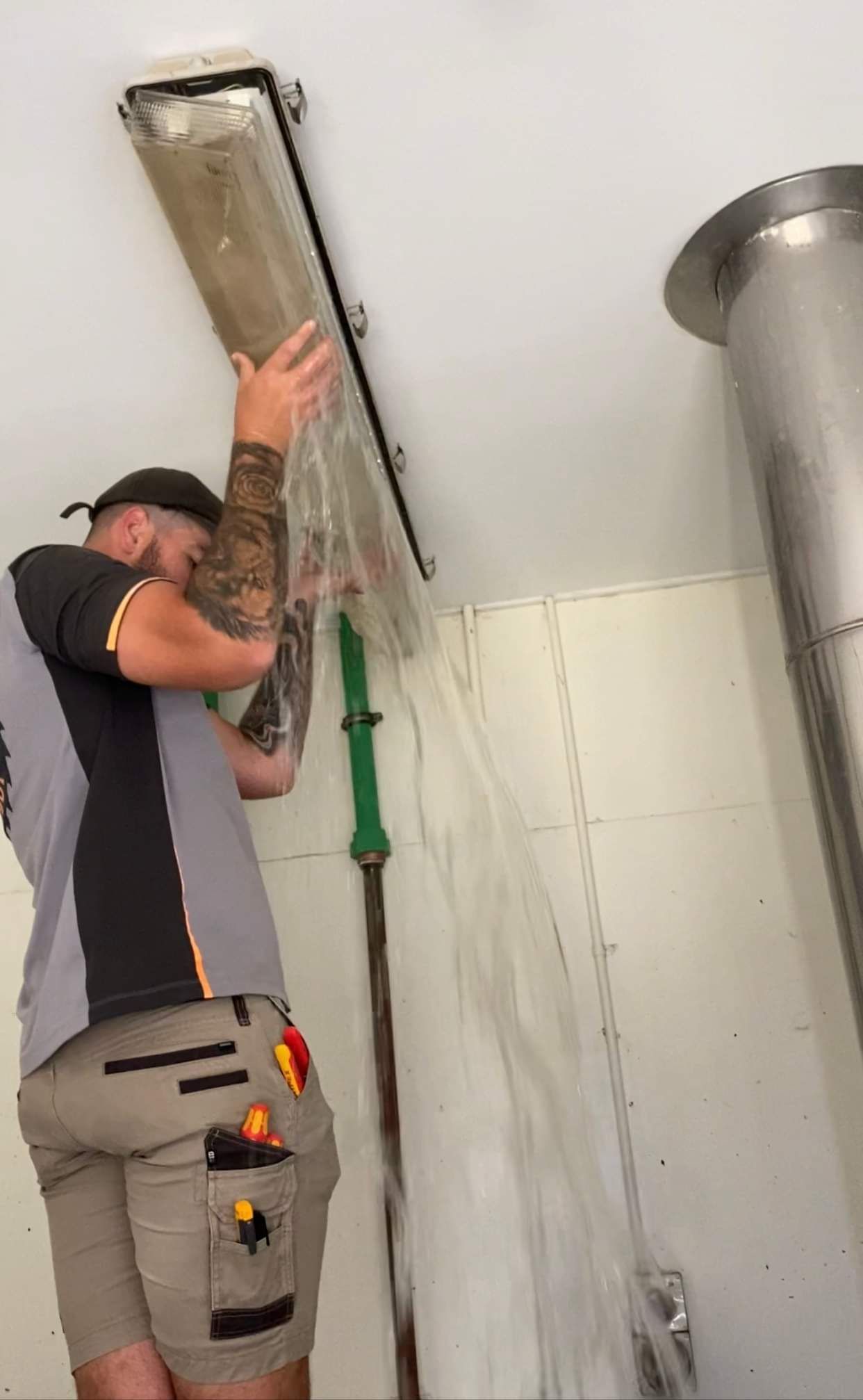 Worker cleaning a ceiling air vent with a long pole in a tiled room