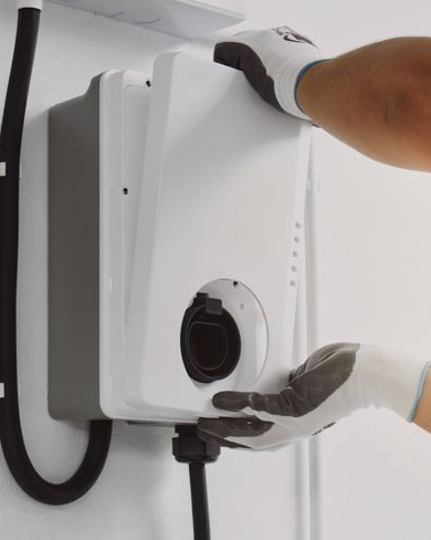 Gloved hands mounting a white wall charger on a wall, with cables attached