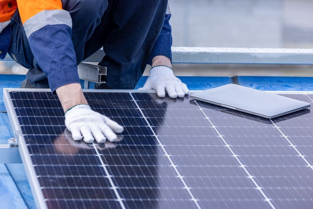 Worker installing solar panels on a rooftop, wearing gloves and an orange safety jacket