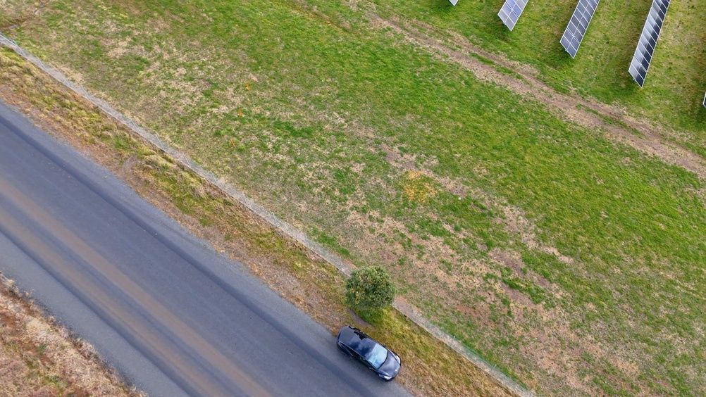 Aerial view of a roadside with a parked car beside a grassy field and solar panels.