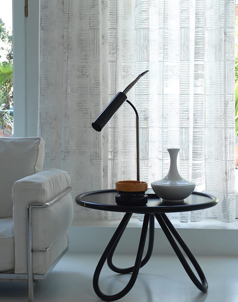 Interno moderno con tavolino nero, vaso bianco, lampada e tenda trasparente.
