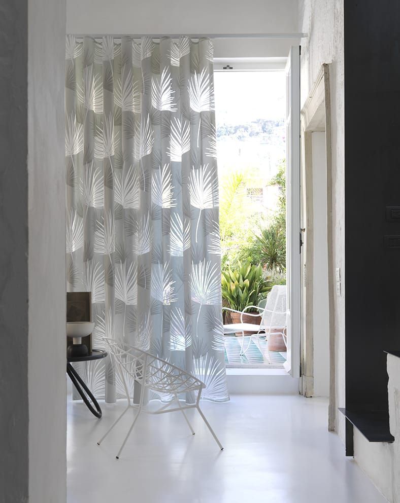 Tenda bianca trasparente con motivo a foglie, porta aperta sul balcone con verde.