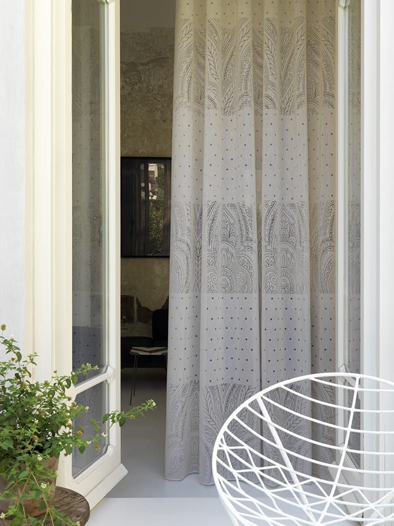 Una tenda trasparente e decorata è appesa a una porta aperta, con una sedia bianca e del verde in primo piano.
