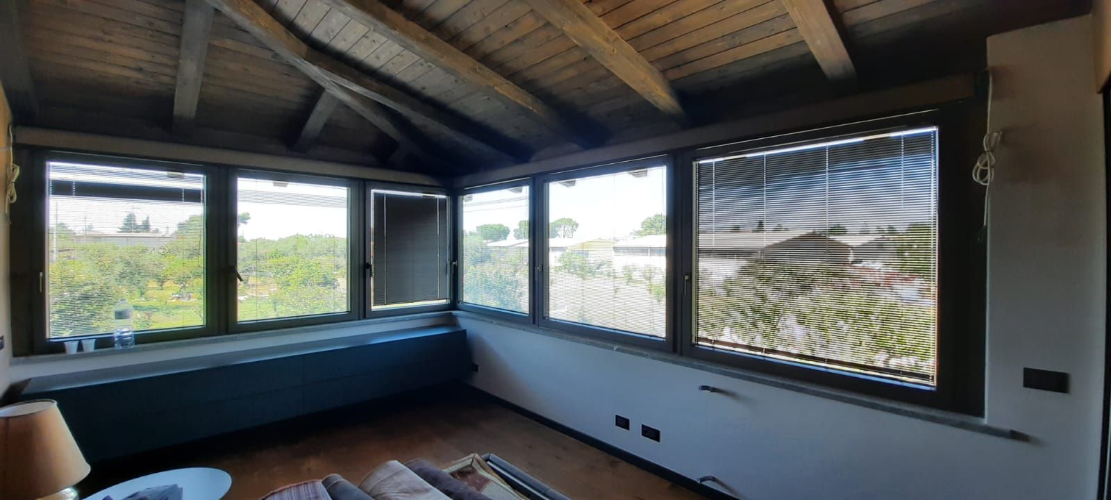 Camera con numerose finestre che si affacciano su un paesaggio verde, soffitto in legno.