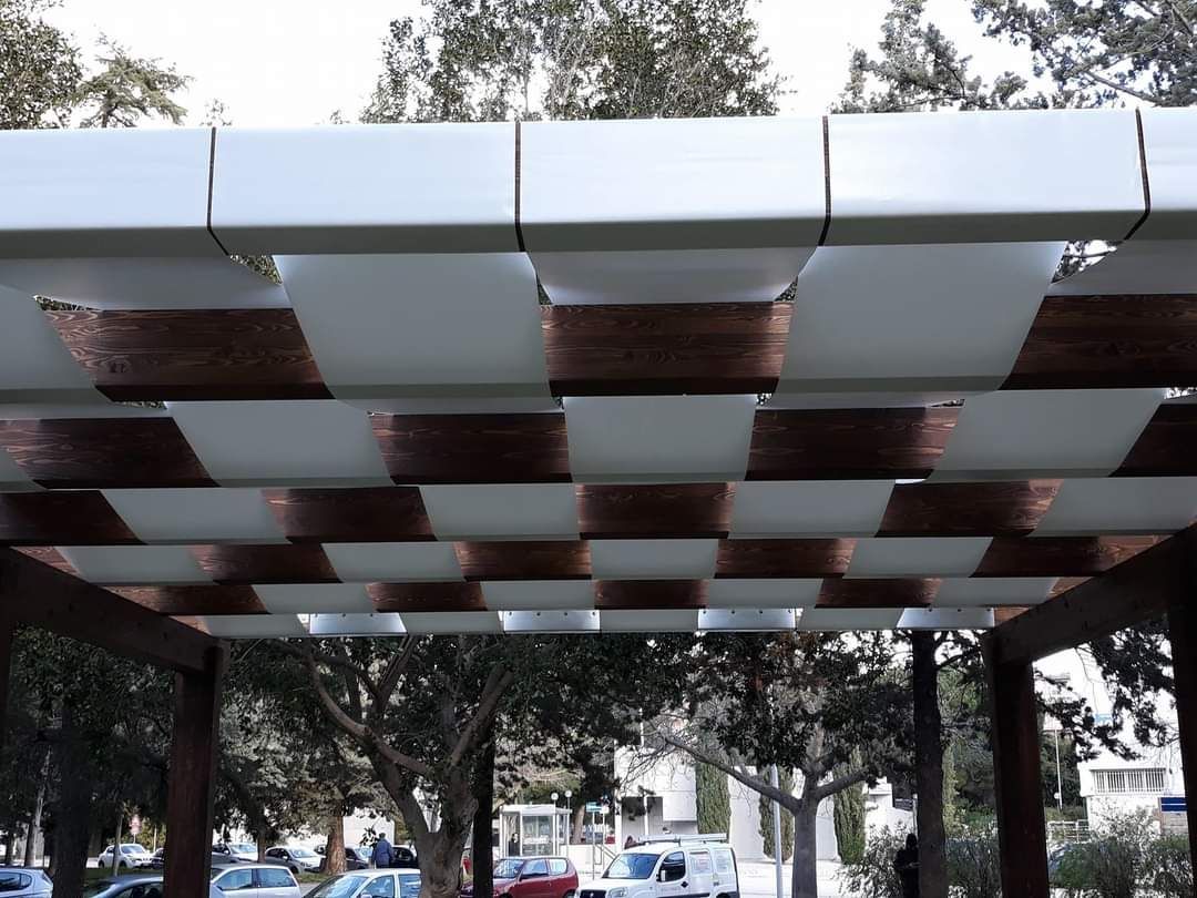 Tetto a pergola intrecciata con pannelli bianchi e color rame. Sullo sfondo si vedono alberi e auto parcheggiate.
