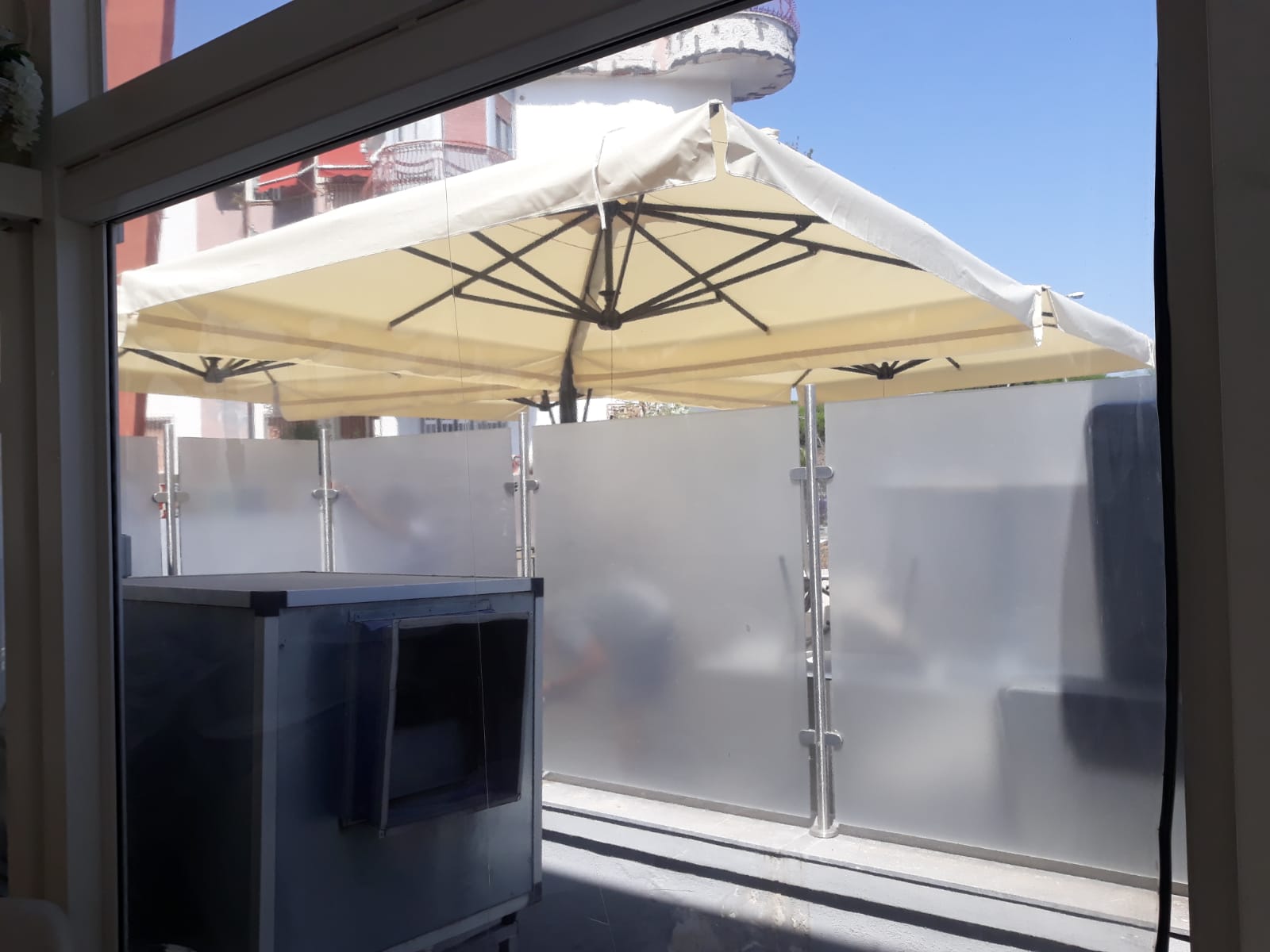 Ombrellone beige da giardino sopra una recinzione in vetro smerigliato. Esterno dell'edificio visibile.