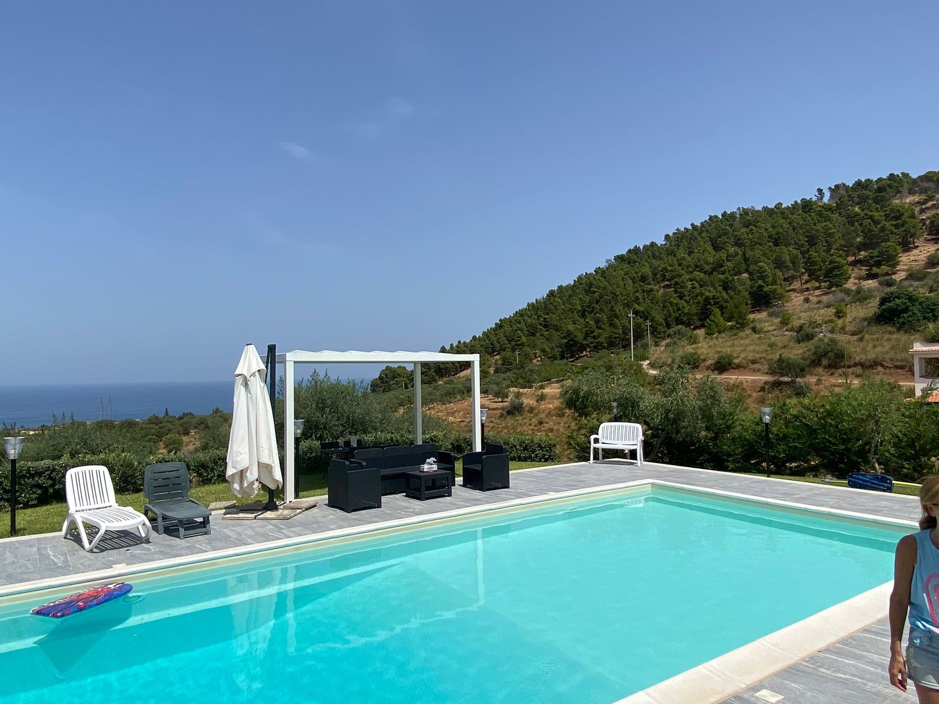 Piscina con vista sull'oceano e sulle colline, posti a sedere all'aperto e area per bambini.