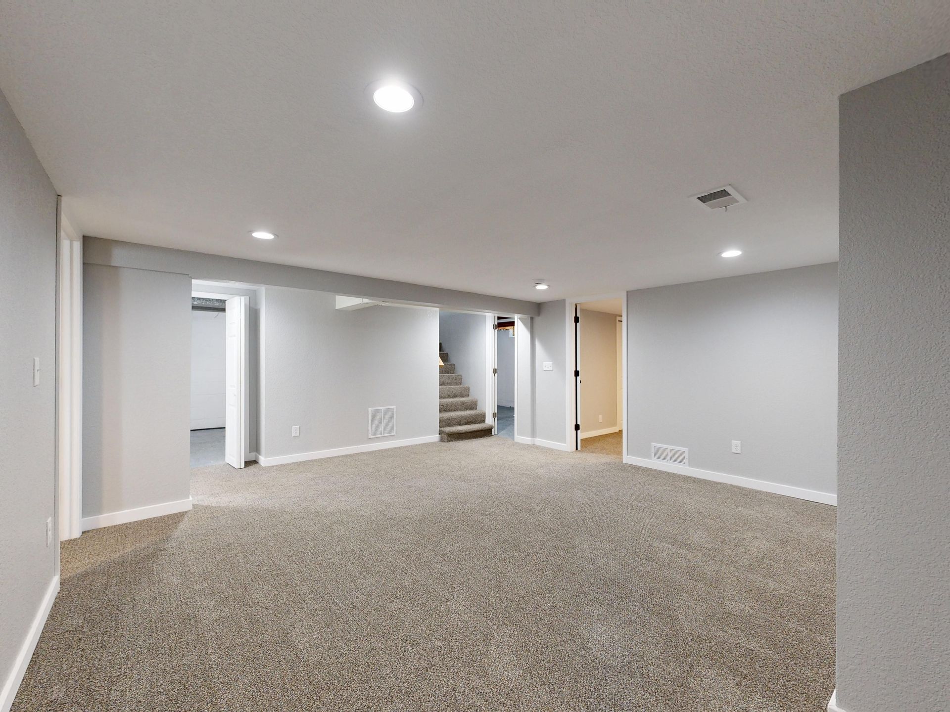 Empty finished basement with carpet, recessed lights, stairs, and gray walls