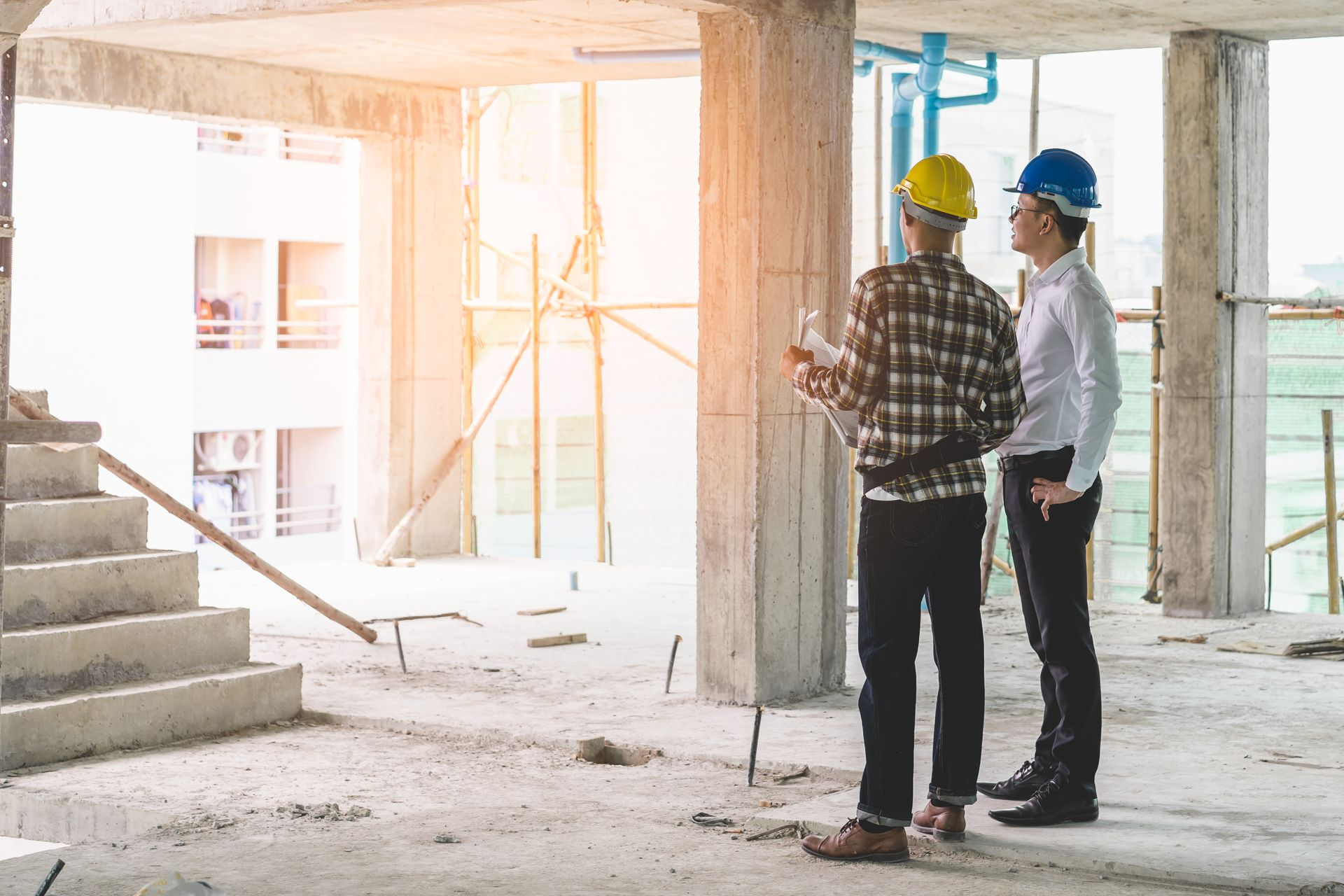 Two construction workers in hard hats inspecting a bright unfinished building interior