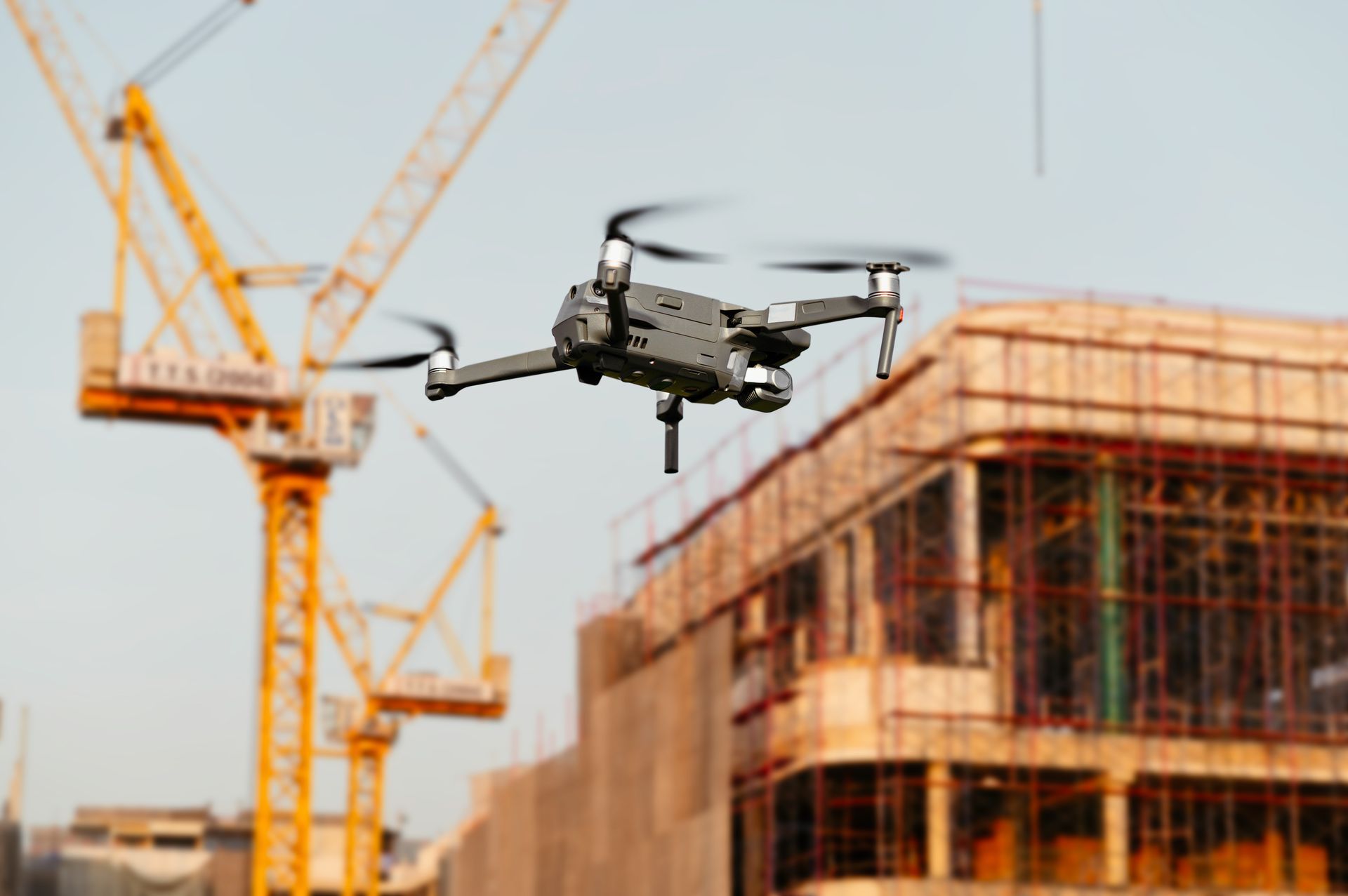 Drone flying above a construction site with cranes and a building under construction
