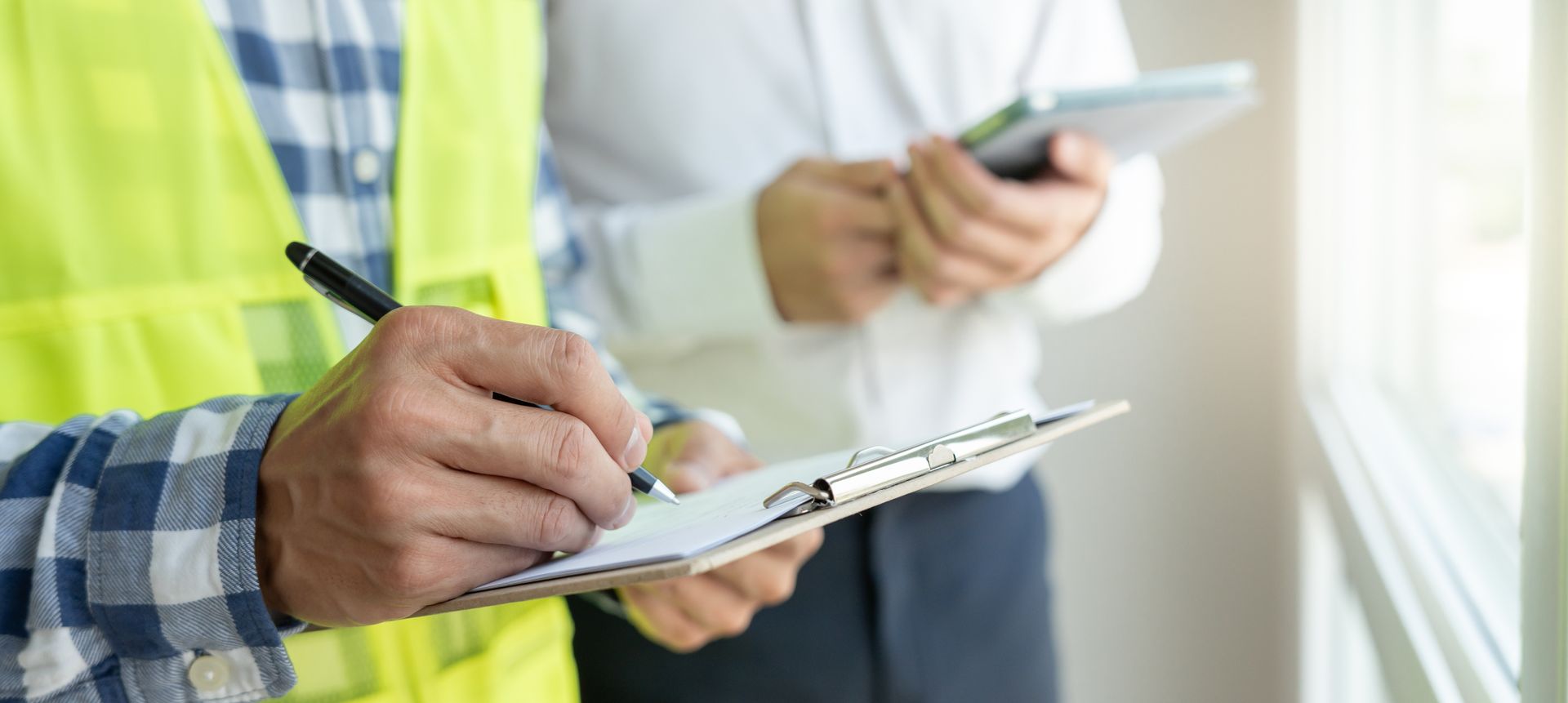 Construction workers using a clipboard and smartphone in a bright worksite setting
