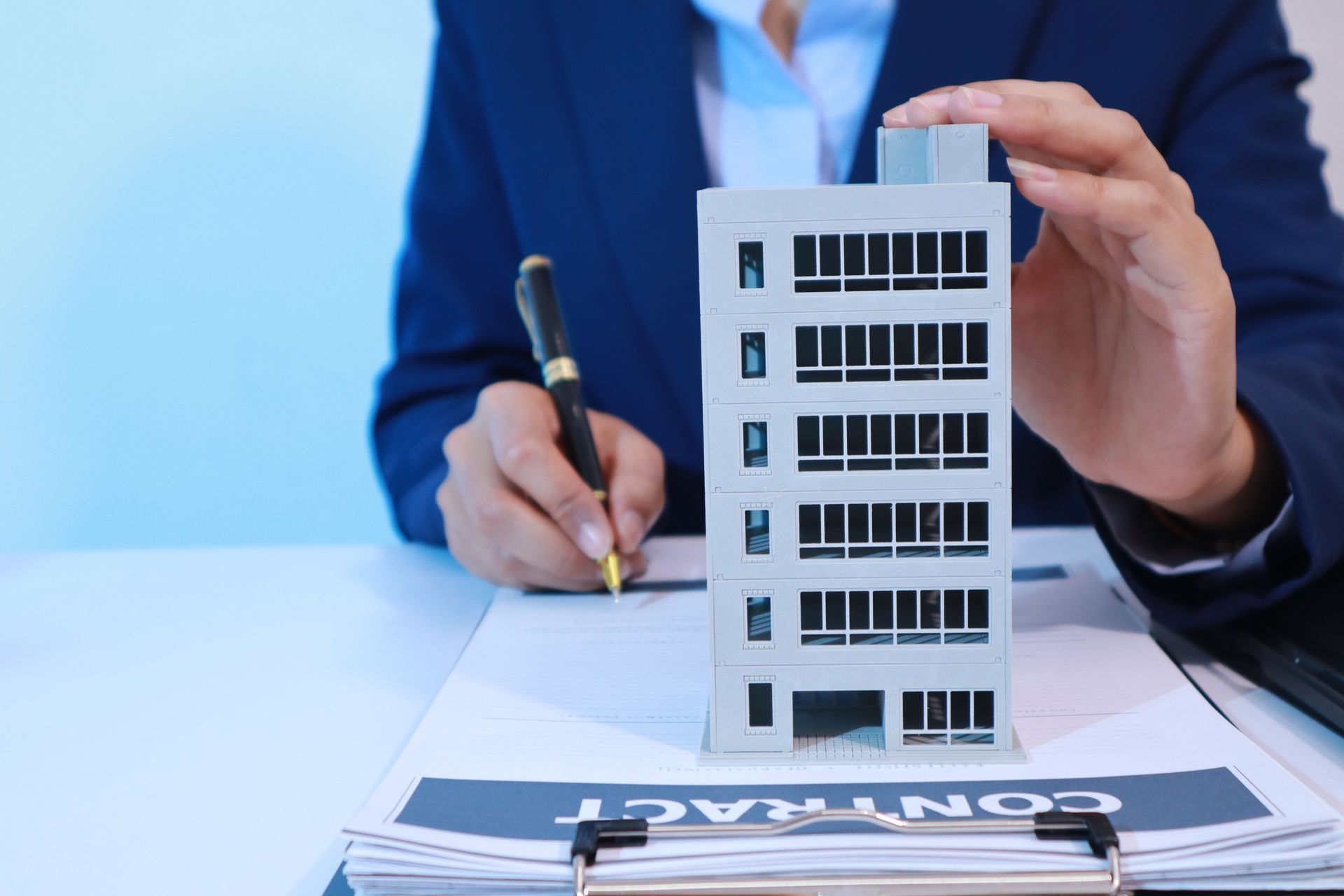 Person in suit holding a model building and pen over insurance paperwork on a desk