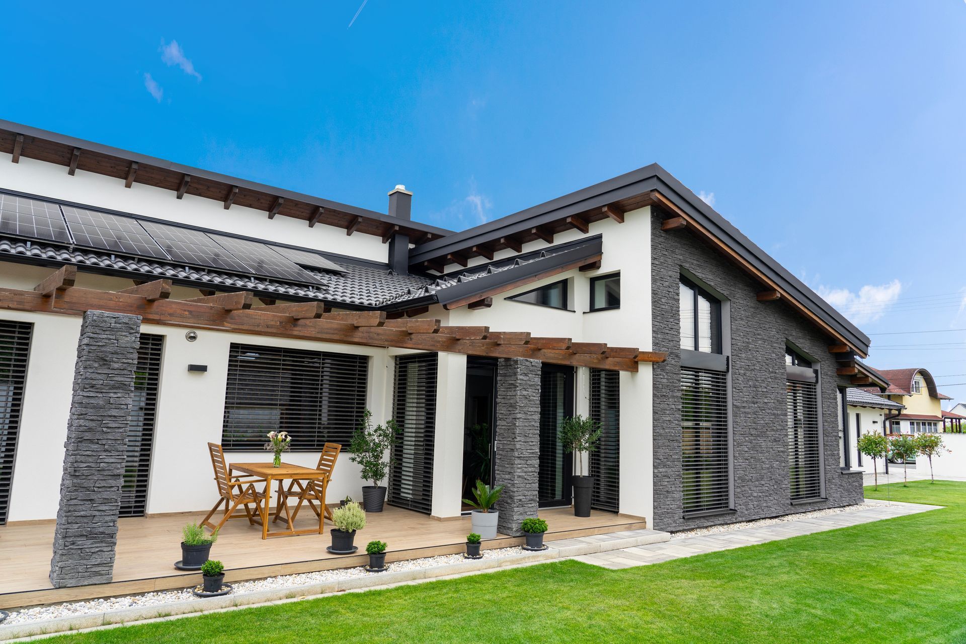 Modern house exterior with stone accents, wooden patio, and green lawn under a blue sky