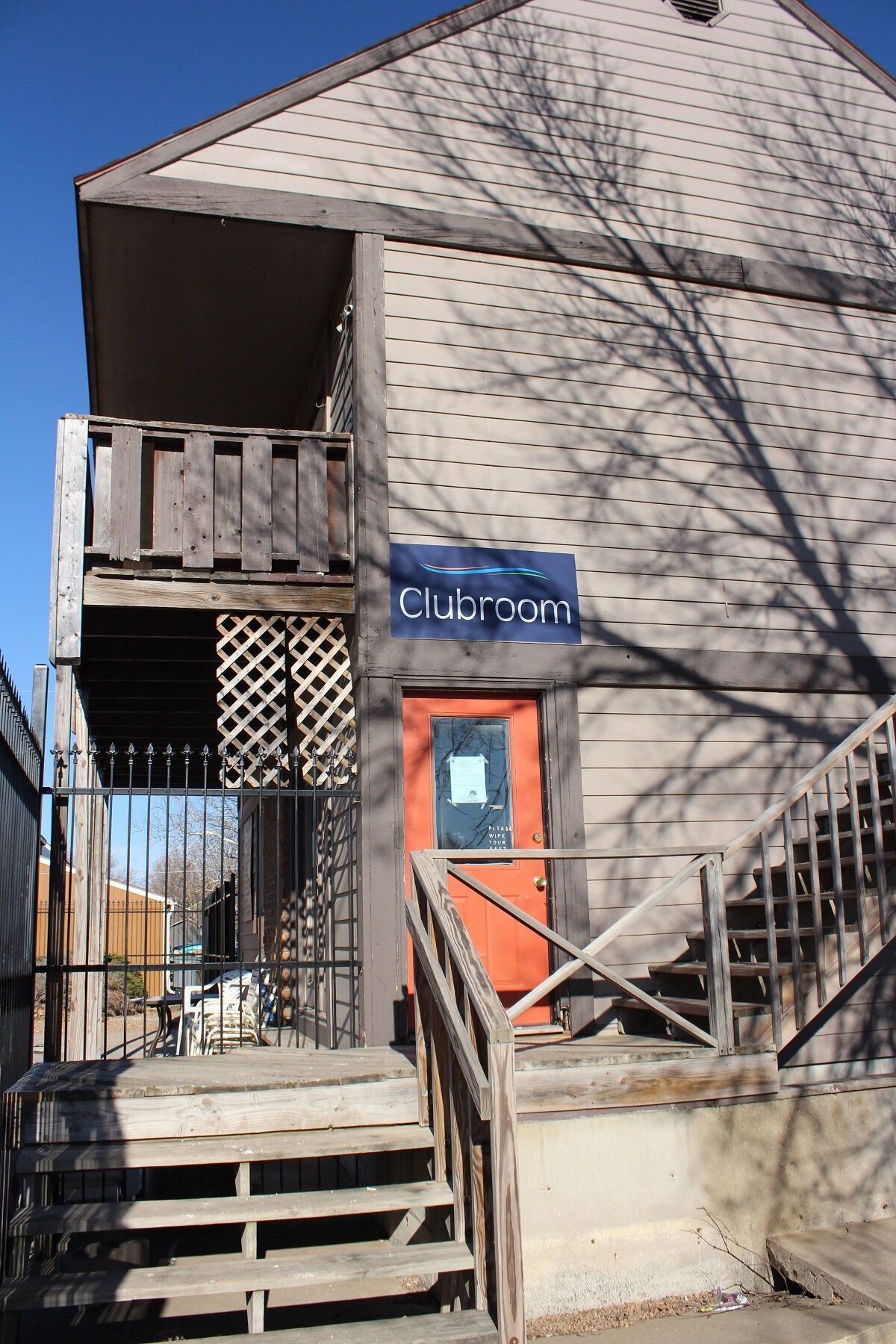 Brown two-story building with stairs, a balcony, and a red door.