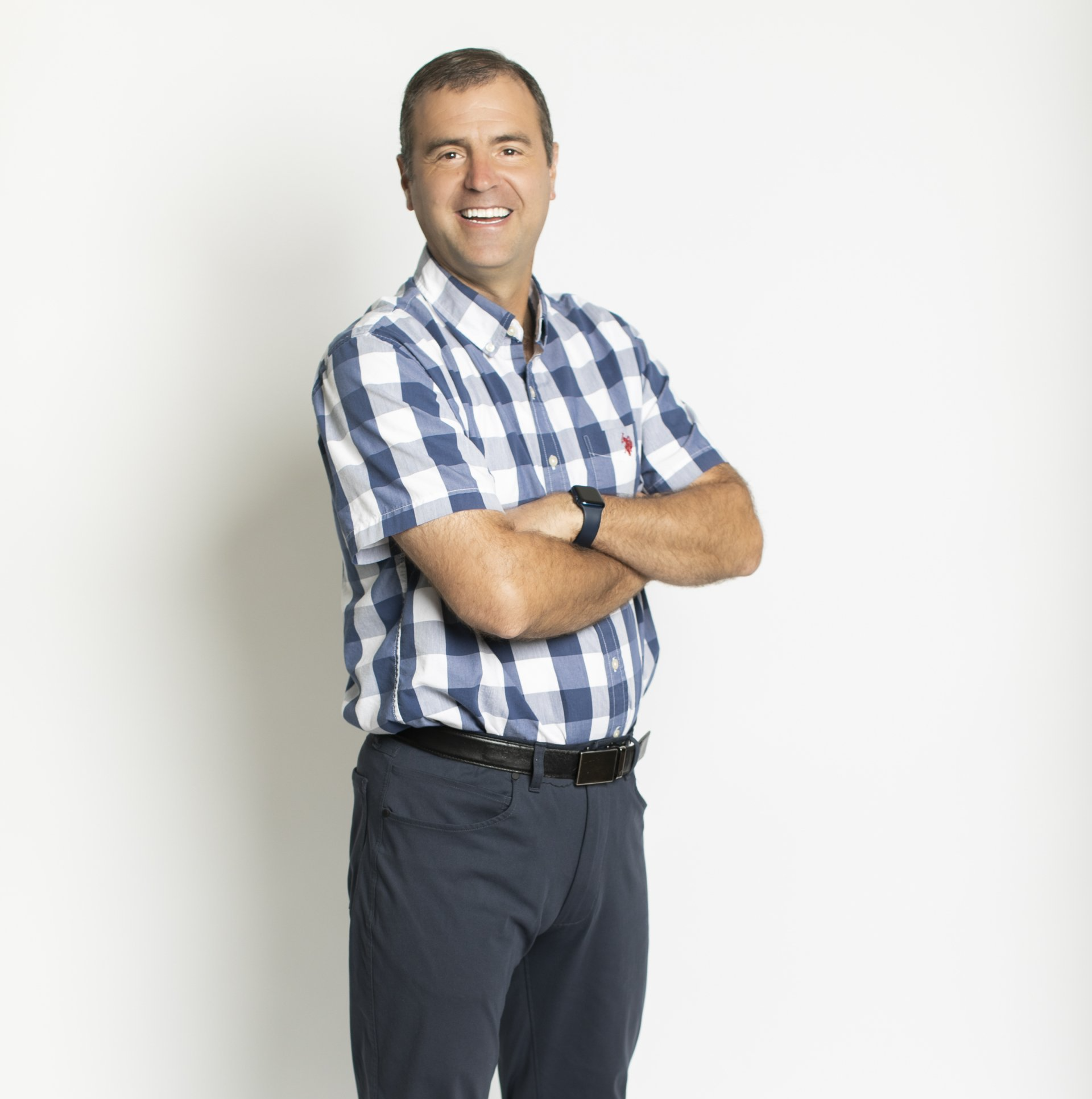 Smiling man in a blue plaid shirt with arms crossed, standing against a white background